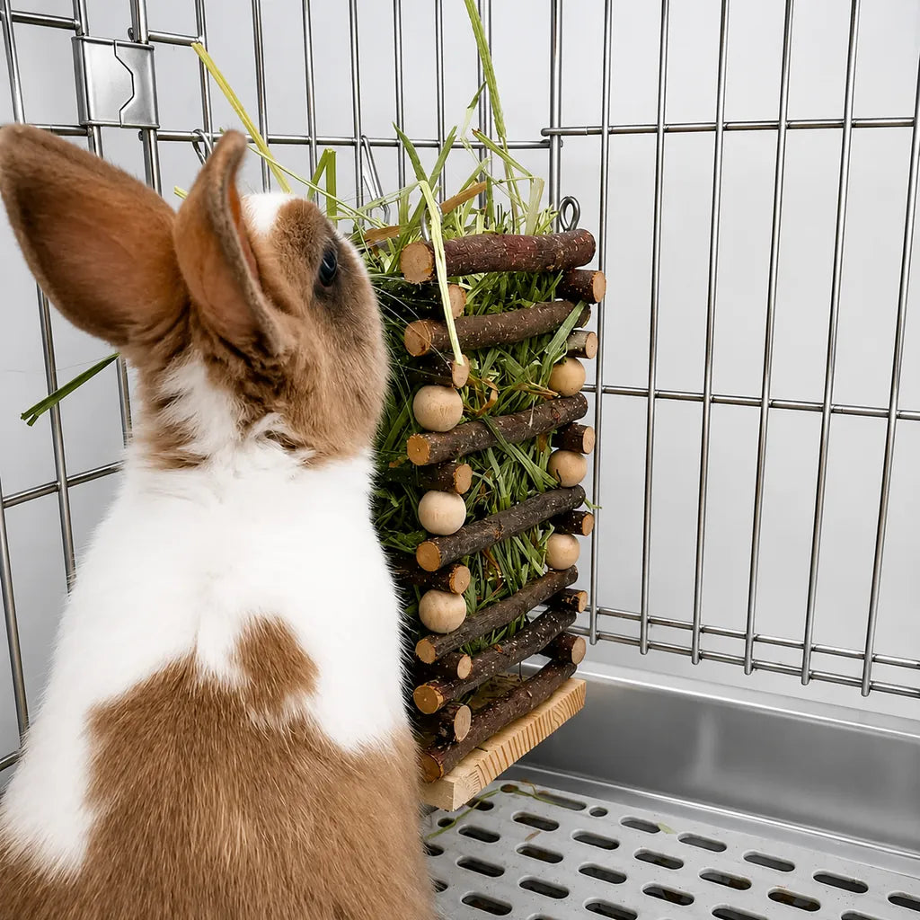 White and brown rabbit using a natural wooden hay feeder inside a metallic pet cage. Durable hanging hay rack for rabbits, guinea pigs, and other small pets to reduce waste and keep hay clean.